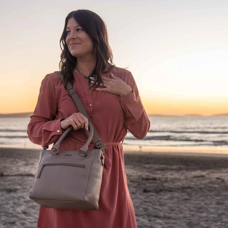 Woman holding a beige handbag on a beach at sunset
