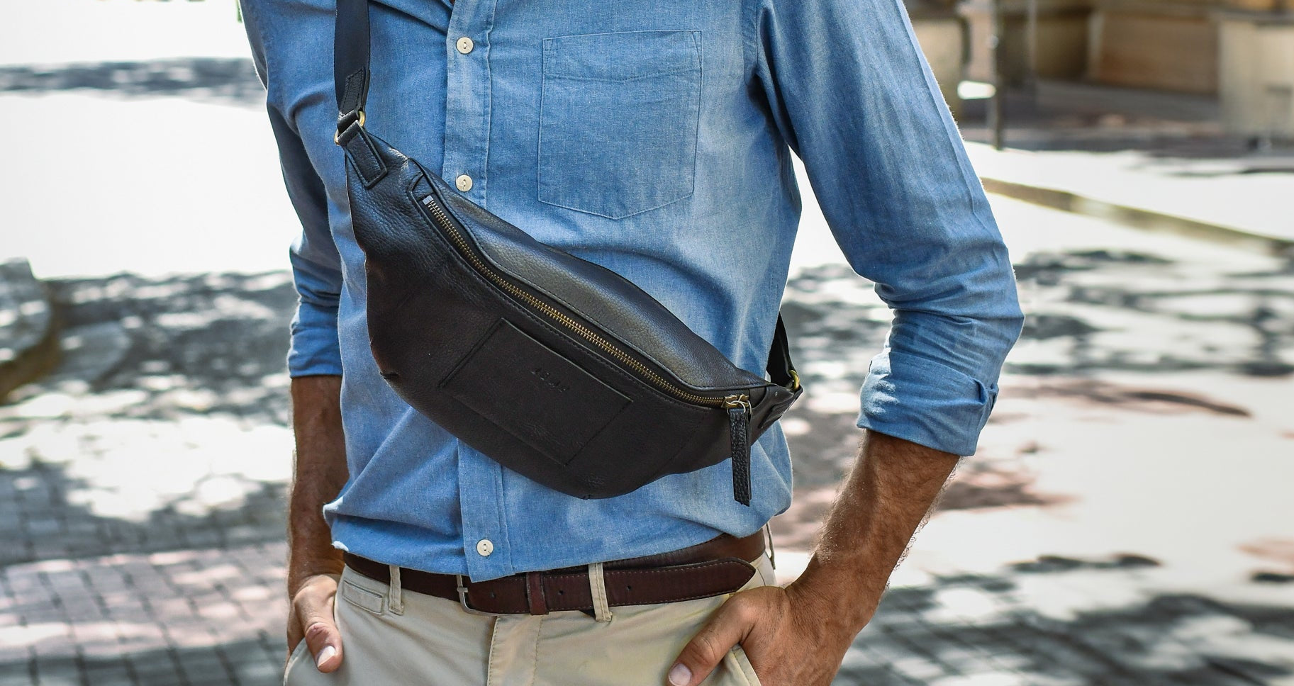 Person wearing a blue shirt and carrying a black waist bag on a street.