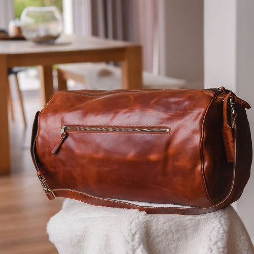 Brown leather duffel bag on a white surface with a blurred indoor background