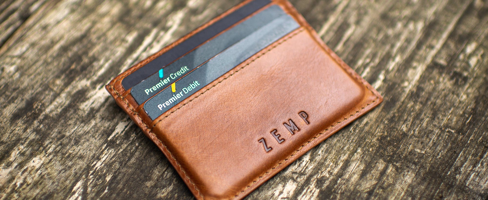 Brown leather wallet with cards on a wooden surface, featuring the brand 'ZEMP'.