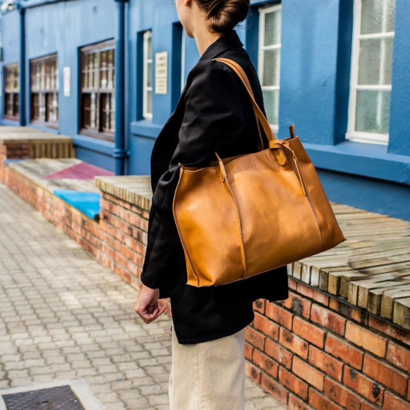 Person holding a brown leather bag in front of a blue building
