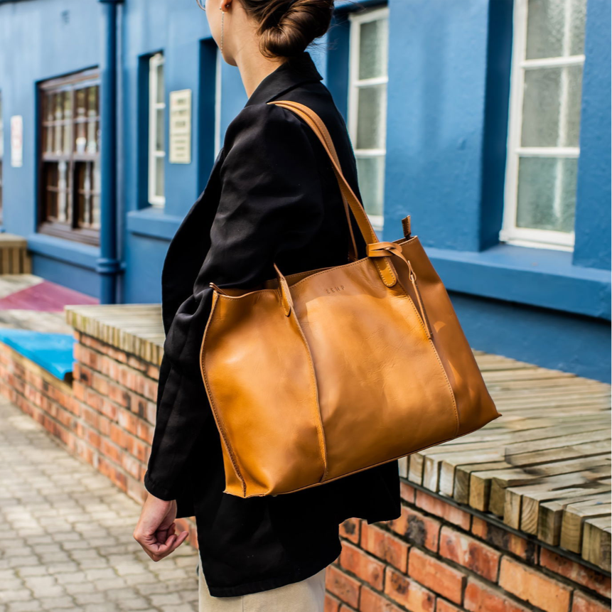 Person holding a brown leather bag in front of a blue building